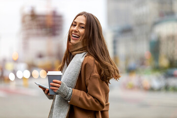 Wall Mural - smiling young woman with smart phone and coffee cup outdoors at urban setting