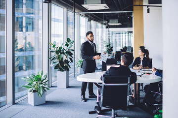 Wall Mural - Hispanic businessman making training conference meeting with male and female employees explaining strategy information from corporate report, group of experienced people discussing productive teamwork