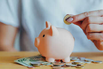 the woman's hand puts a coin in a pink piggy bank standing on the table. Concept of saving money or savings, investment during the global crisis