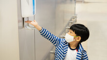 New Normal Behavior For Kids In The World Of Covid-19. An Asian Little Boy Reaching Hand To An Automatic Contactless Alcohol Dispenser Spray To Sanitize His Hands Often While Traveling. Travel Bubble.