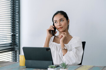 Attractive and successful asian businesswoman working in modern office, talking on phone with client at their desk.