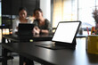 © Prathankarnpap - A white screen computer tablet is putting on black wooden table in meeting room with blurred two businesswoman background.