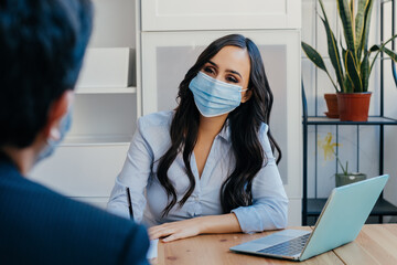 Portrait of a business woman at meeting sitting at desk with client wearing face mask for social distancing due to coronavirus