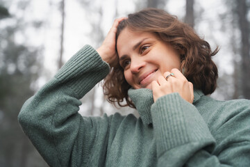 Wall Mural - Happy young beautiful woman in warm cozy green sweater in beautiful foggy pine forest