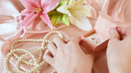 Wall Mural - hand takes box with ring near pearls necklace and flowers on pink background, wedding ring, closeup