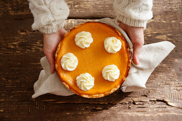 Wall Mural - Traditional thanksgiving food concept. Woman in white knitted sweater holding a delicious homemade pumpkin pie with crust. Top view, close up, copy space, background