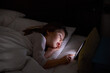 © Q - six years old girl lying on white bed at night touching digital screen mobile phone