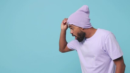 Wall Mural - Shocked amazed young african american man 20s wearing violet t-shirt hat glasses isolated on blue turquoise background in studio. People lifestyle concept. Looking aside keeping mouth open say wow