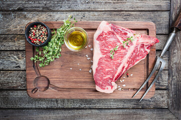 Wall Mural - Raw T-bone Steak with fresh herbs and oil on dark wooden background, top view