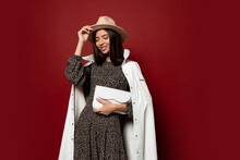 Autumn Fashion Look. Studio Image Of Gorgeous European Brunette Gir In Trendy White Jacket And Dress With Print Posing On Red Background. Holding Leather Handbag.