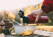 Early morning picnic in forest in late autumn. Cookies and hot tea woman pouring from thermos bottle on wooden table.