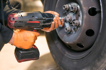 Wall Mural - Car mechanic worker doing tire or wheel replacement with electric wrench in garage of repair service station. High quality photo