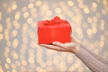 Woman holding a red gift box with a red bow on a bright holiday lights background