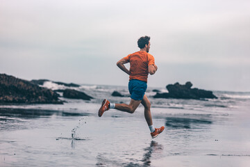 Wall Mural - Exercise outdoor athlete man running on wet sand at beach training cardio sprinting fast. Profile of runner in sportswear clothes jogging.