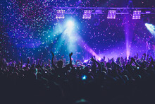 A Crowded Concert Hall With Scene Stage Lights, Rock Show Performance, With People Silhouette, Colourful Confetti Explosion Fired On Dance Floor Air During A Concert Festival