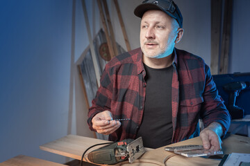 Poster - The master holds a saw in his hands and looks past the camera. A man picks up a suitable saw. Attachment for an electric jigsaw. Woodworking tool. Blades for jig saw. Woodworking.