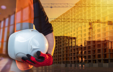 Urban construction. Construction of houses. The figure of a construction worker in work gloves with a white helmet under his arm. Apartments in new buildings.