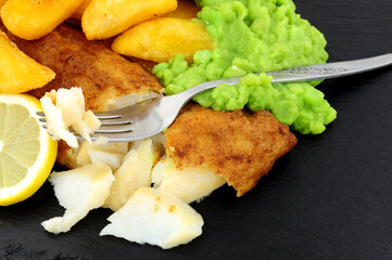 Wall Mural - Battered cod fish fillet with chunky chips and mushy peas on a slate stone background