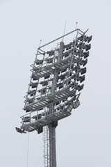 Stadium floodlight with metal pole, lighting mast, tower with floodlights in the sports stadium against the white sky.