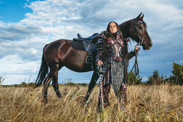 Wall Mural - Knight woman in armor with a horse against the sunset fields background