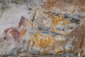 Close-up view of volcanic rock with red and yellow sulfur incrustations