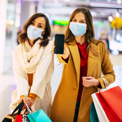 Wall Mural - Two young girl friends in safety medical masks during shopping in the mall