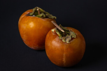 Persimmon on a black background. Two persimmons lie next to each other. Healthy fruits