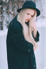 Poster - Stylish beautiful blonde girl in black clothes and hat posing near fence in the street