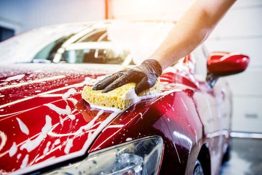 Worker washing red car with sponge on a car wash