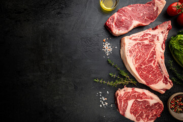 Wall Mural - Variety of Fresh Raw Black Angus Prime Meat Steaks T-bone, New York, Ribeye and seasoning on black background, top view