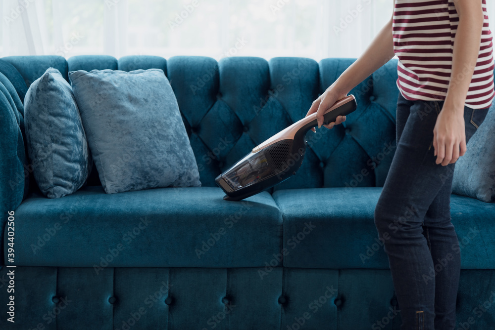 Woman housewife vacuuming furniture in a house with a hand-held portable vacuum cleaner - obrazy, fototapety, plakaty 