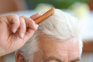 Wall Mural - Senior man combing his hair at home, closeup