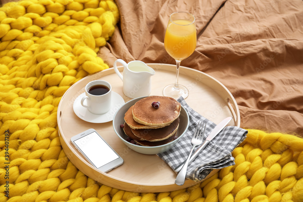 Tray with tasty breakfast and mobile phone on bed