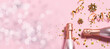 © Iryna - Long wide Christmas and New Year’s banner with rose Champagne bottles, golden decorations and bokeh lights on pink pastel background. Festive party banner template with copy space for your text.
