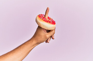 Wall Mural - Finger of hispanic man holding donut over isolated pink background.