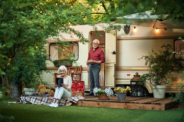 Beautiful elderly woman looking at gadget screen and sitting on the van porch