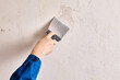 Repairman is finishing wall at home with putty and work tool.