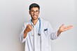 © Krakenimages.com - Young handsome man wearing doctor uniform and stethoscope amazed and smiling to the camera while presenting with hand and pointing with finger.