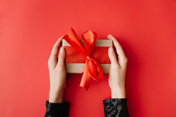 Woman hands holding present box with red bow on red background. Flat lay, top view, copy space.