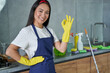 © Friends Stock - Under control. Portrait of joyful young woman, cleaning lady wearing protective gloves, smiling and showing OK sign while getting ready for cleaning the house