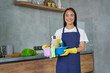 © Friends Stock - Consider it clean. Happy young woman, cleaning lady smiling at camera, holding container full of cleaning supplies and equipment while standing in the modern kitchen