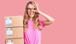 © Krakenimages.com - Young caucasian woman with blond hair holding delivery package smiling happy doing ok sign with hand on eye looking through fingers