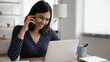 © fizkes - Close up smiling Asian woman talking on phone, using laptop, sitting at work desk, happy businesswoman negotiating project with business partner, friendly manager consulting client, making call