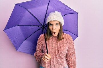 Canvas Print - Young caucasian woman holding purple umbrella smiling with an idea or question pointing finger with happy face, number one