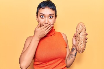 Sticker - Young woman holding wholemeal bread covering mouth with hand, shocked and afraid for mistake. surprised expression