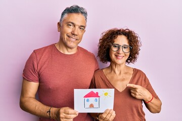 Sticker - Beautiful middle age couple holding house draw buying home for the future smiling happy pointing with hand and finger