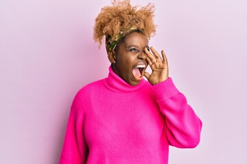 Poster - Young african woman with afro hair wearing casual winter sweater shouting and screaming loud to side with hand on mouth. communication concept.