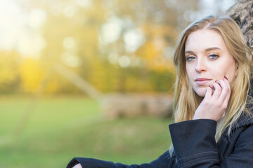 Cool young woman is posing in the autumn park looking at the camera. Horizontally. 