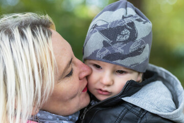 Closeup view of young grandmother kissing on the cheek her little grandson outdoors.