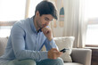© fizkes - Pondering over answer. Pensive millennial businessman holding cellphone in hands thinking on offer proposal received by email, thoughtful young man looking on phone screen hesitating about making call